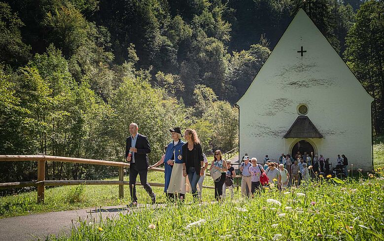  Menschen auf einem Weg, der von einer Kapelle wegführt